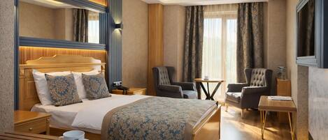 A hotel room with a large bed, two armchairs, a small table, and a TV.