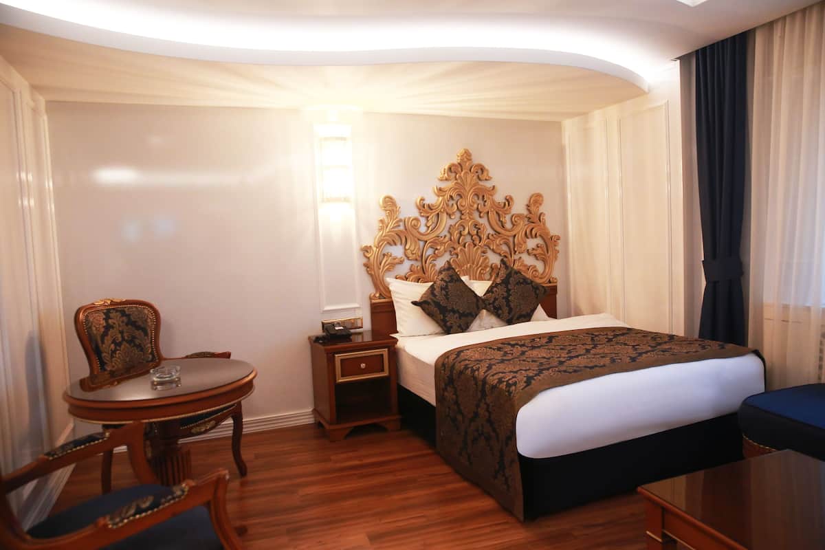 A hotel room with a large bed, a wooden nightstand, a chair, and a small table.