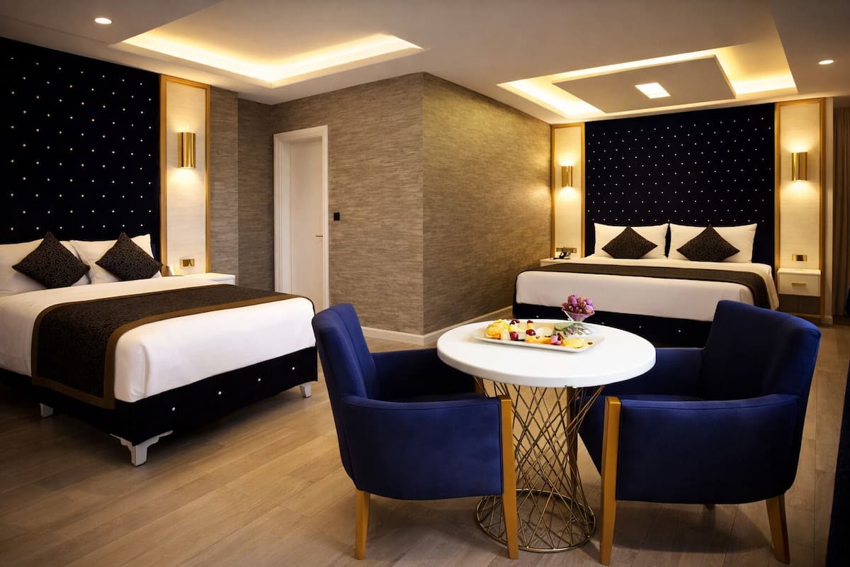 A hotel room with two beds, a round table with a fruit platter, and a night sky wall design.