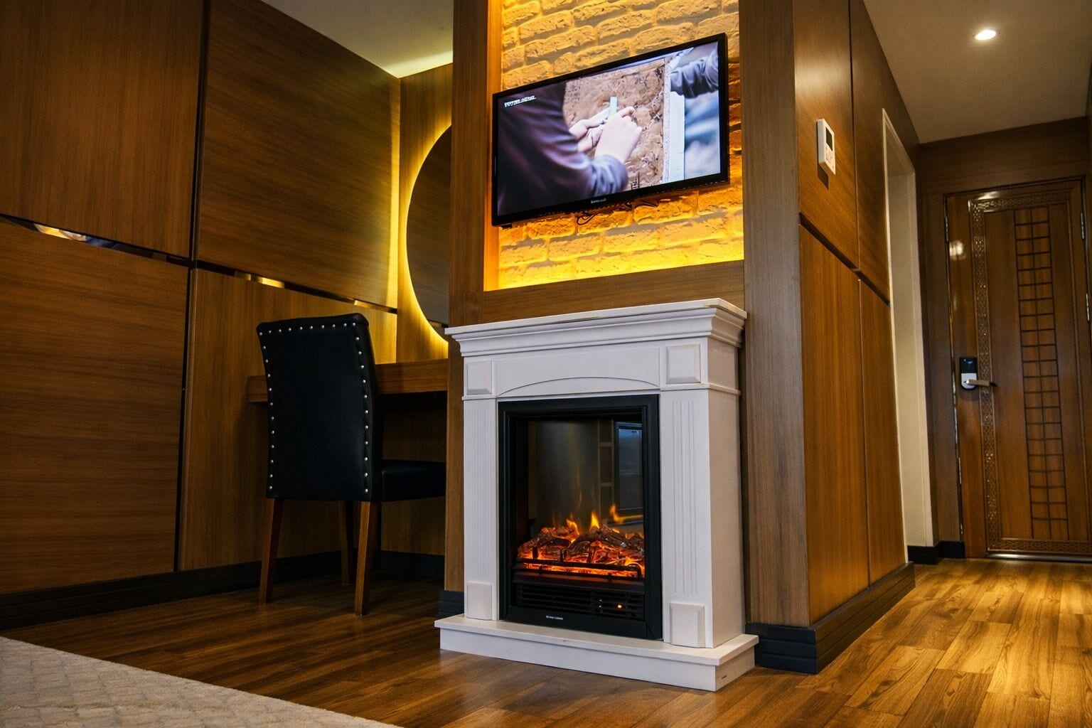 A modern interior with a fireplace, a television mounted on a brick wall, and a wooden floor.