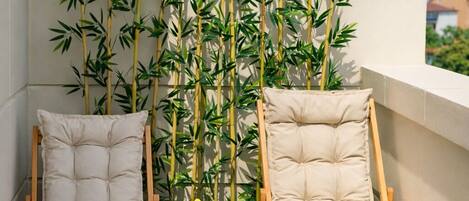 Dos sillones de madera con cojines, una mesita con frutas y bebidas, y una pared decorativa de bambú.