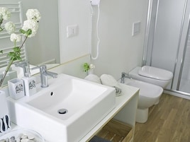 Un baño moderno con un lavabo blanco grande, un cabezal de ducha de mano, un inodoro y un espejo.