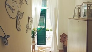 A narrow hallway with wooden flooring, a white door with green shutters, and a refrigerator on the right. - Altamarea (La Spezia)
