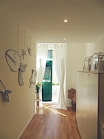 Un pasillo estrecho con suelo de madera, una puerta blanca con contraventanas verdes y un refrigerador a la derecha.