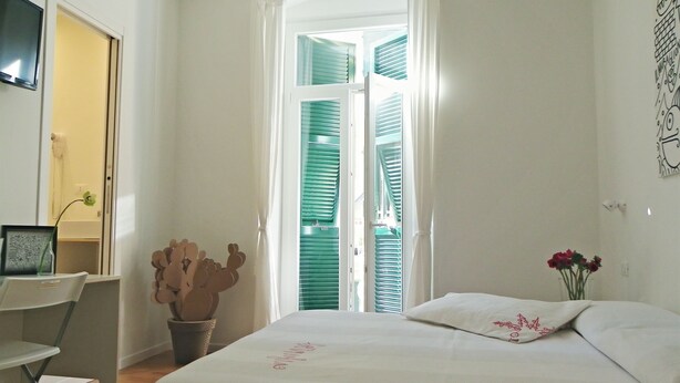 A hotel room with a bed, a desk, a chair, a vase with flowers, and a window with shutters. - Altamarea (La Spezia)