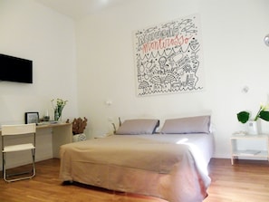 A bedroom with a bed, a desk, and a chair. There is a wall art piece above the bed. - Altamarea (La Spezia)