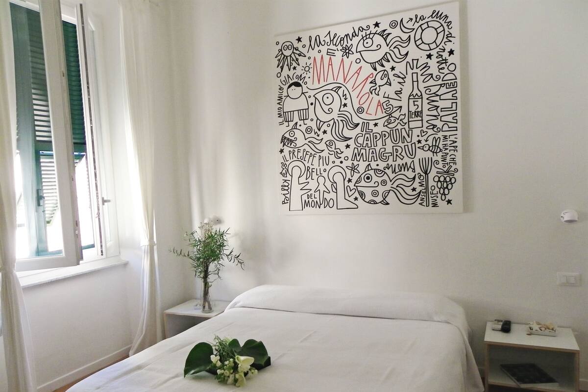 Ein Schlafzimmer mit Bett, Nachttisch, Fenster mit Vorhängen und einer Wand mit einer schwarz-weißen Stadtansicht.