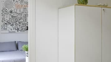 A minimalist room with a white wardrobe, a bed with grey bedding, and a wall with a black and white abstract artwork.