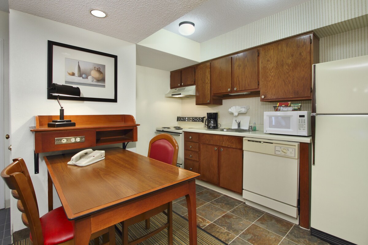A compact kitchen with wooden cabinets, a white refrigerator, a microwave, a coffee maker, and a telephone on the table.