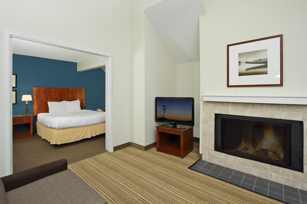 A hotel room with a bed, a television, a fireplace, and a framed picture on the wall.