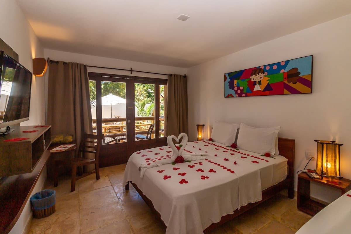 A hotel room with a bed, a desk, a TV, a painting, and a view through the window.