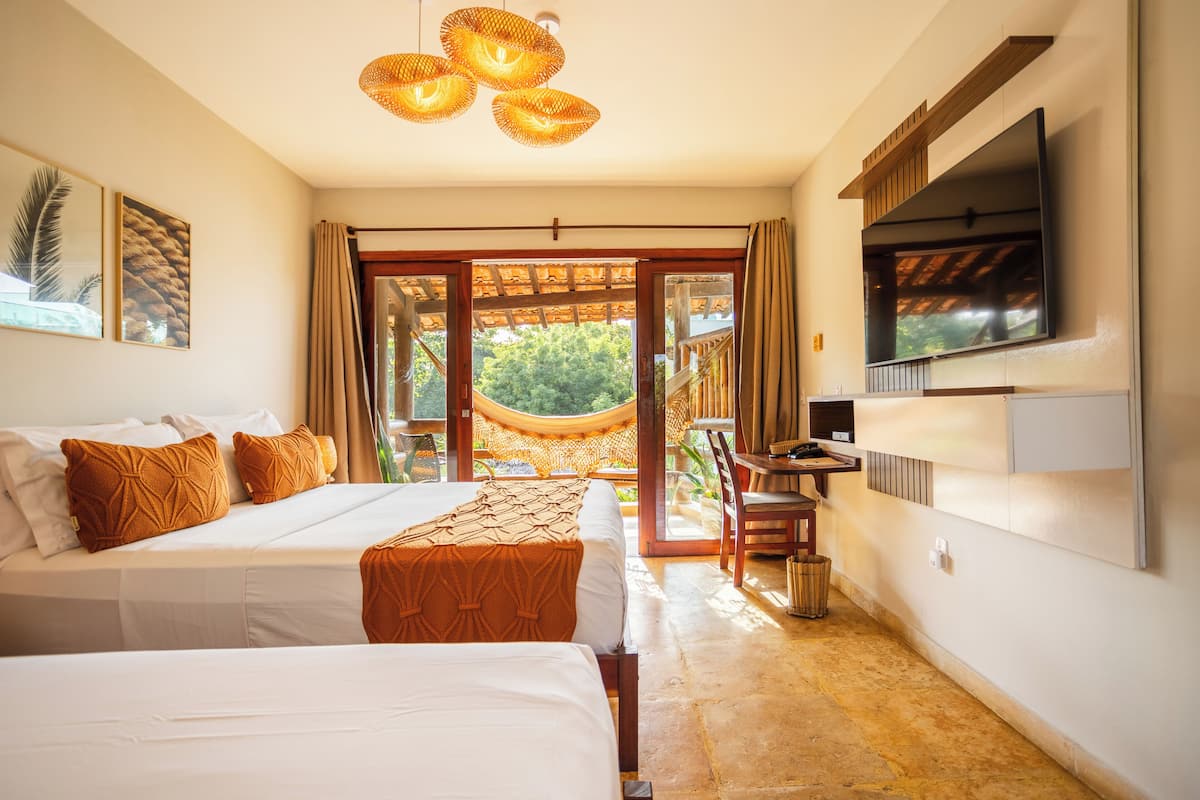 A hotel room with two beds, a TV mounted on the wall, and a hammock outside the door.