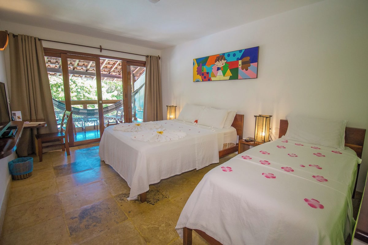 A hotel room with two beds, a hammock, a desk, and a large window with curtains.