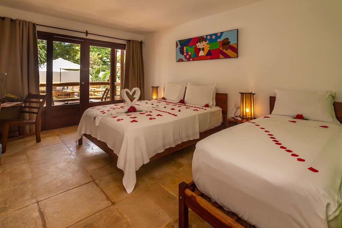 A hotel room with two beds, a dining area, and a view through a glass door.