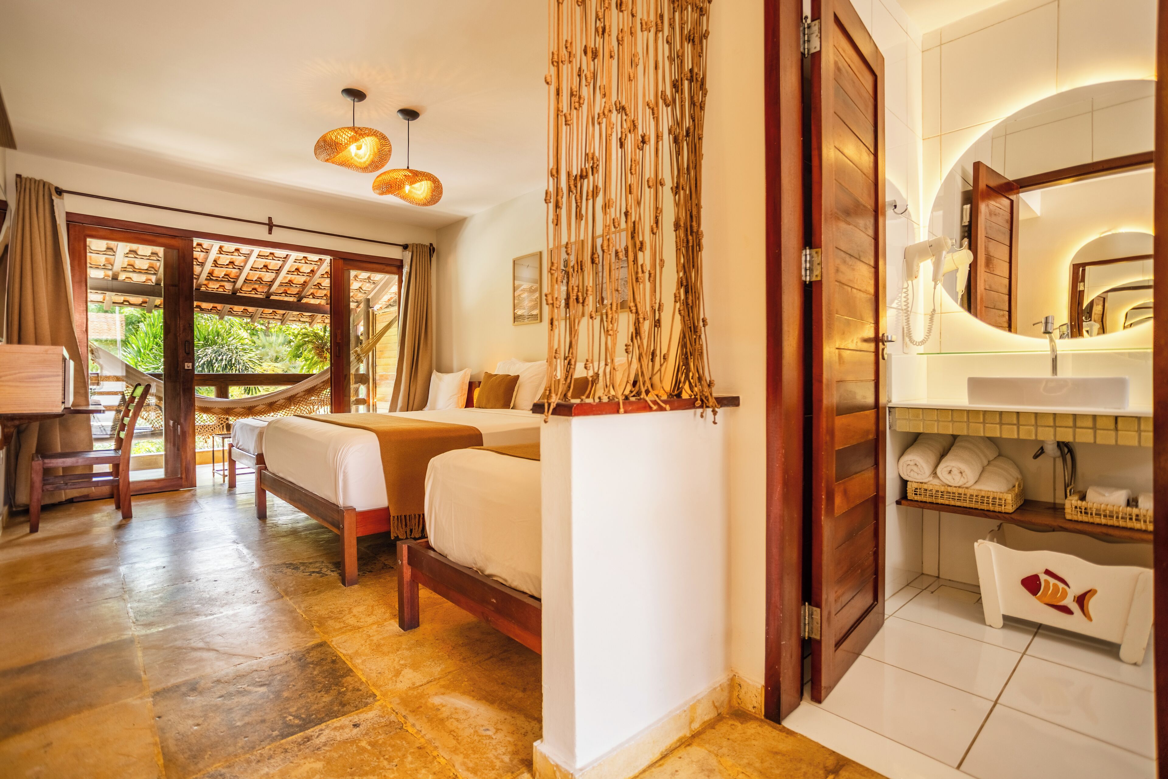 A bedroom with a bed, a desk, and a chair. There is a bathroom with a sink, a mirror, and a towel rack.