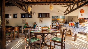 Un comedor rústico con mesas y sillas de madera, techo con vigas a la vista y obras de arte en las paredes.