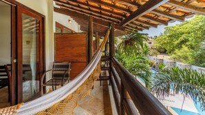 Un balcón con una hamaca, barandas de madera y vista a una piscina.
