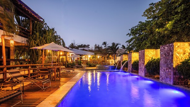 Un área de piscina con sillones de descanso y sombrillas, rodeada de muros de piedra y plantas tropicales.
