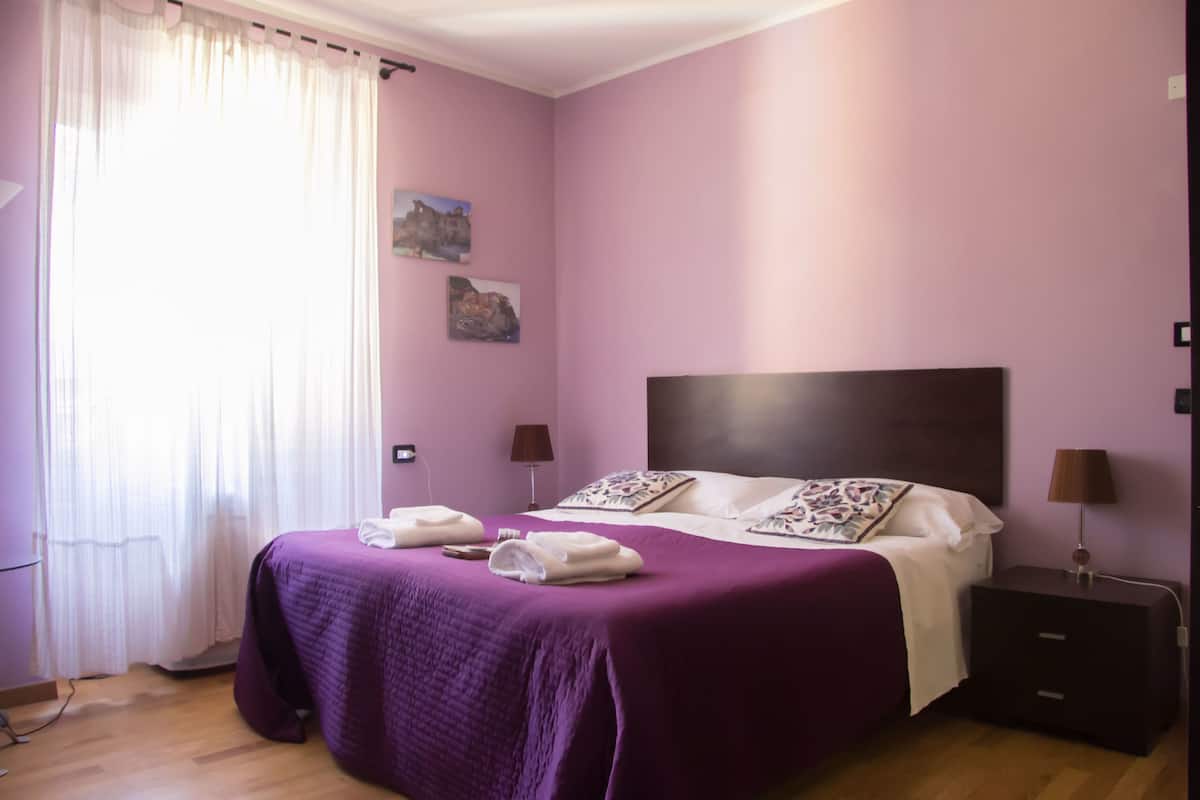 Une chambre à coucher avec un grand lit, deux tables de chevet et une fenêtre avec des rideaux.