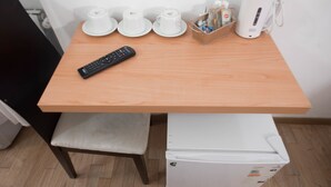 Una kitchenette pequeña con una mesa de madera, un refrigerador blanco, una silla negra y un control remoto.