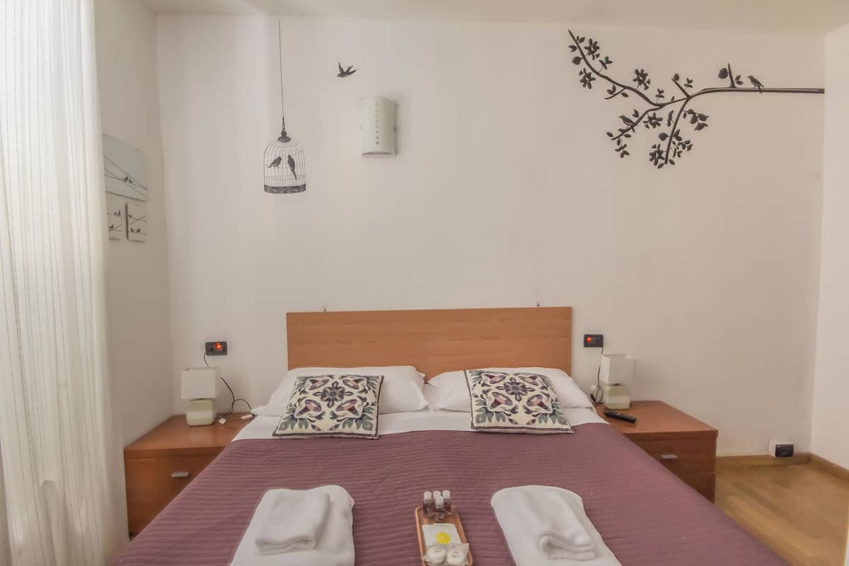 Une chambre à coucher bien aménagée, avec une tête de lit en bois, deux tables de chevet avec des lampes, des œuvres d’art décoratives accrochées au mur et un plateau contenant des articles de toilette.