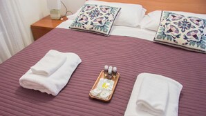 Una cama bien hecha con una colcha morada, dos toallas blancas dobladas y una bandeja con artículos de aseo.
