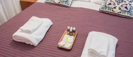 Un lit bien fait, recouvert d’une couverture violette, avec deux serviettes blanches pliées et un plateau contenant des articles de toilette.