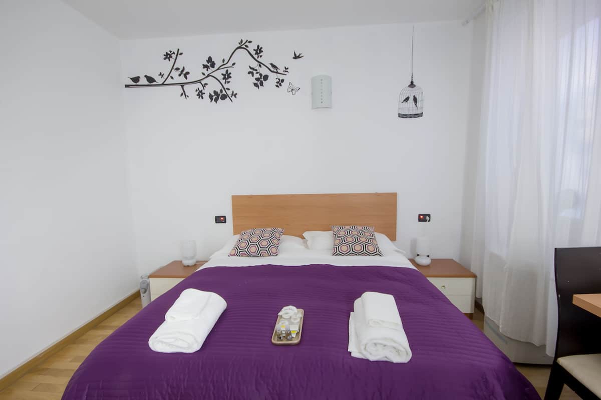 Un lit bien fait, recouvert d’une couvre-lit violette, avec deux oreillers à motifs géométriques et un plateau contenant des articles de toilette.