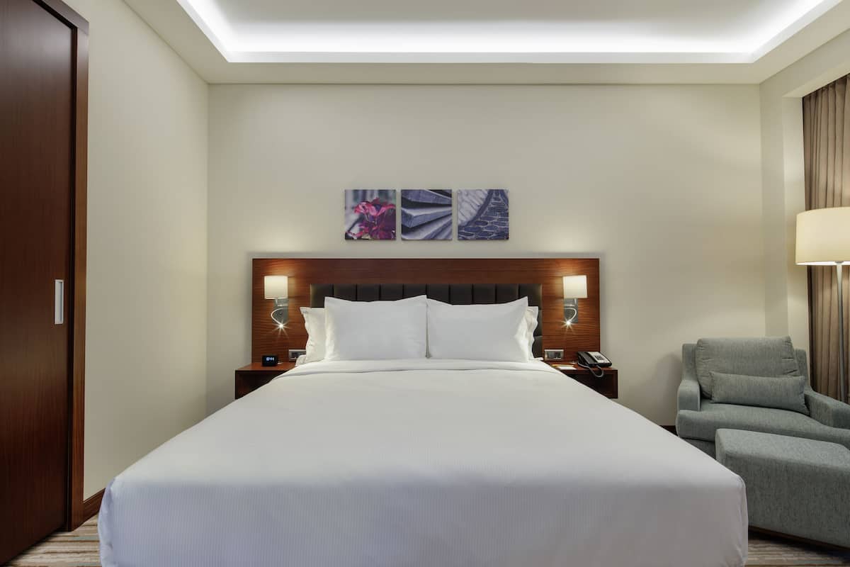 A hotel room with a large bed, two bedside tables with lamps, a chair, and a wall-mounted artwork.
