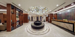 A modern hotel lobby with a central circular seating area, wooden paneling, and a decorative ceiling light fixture. - Hilton Garden Inn Corlu (Corlu)