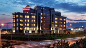 Un hotel de varios pisos con un llamativo letrero de "Hilton Garden Inn", que presenta un diseño arquitectónico moderno con varios balcones y una fachada bien iluminada.