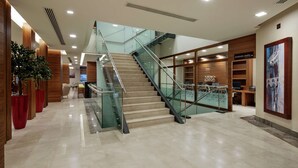 Un moderno vestíbulo de hotel con una escalera de cristal, paneles de madera y una recepción.