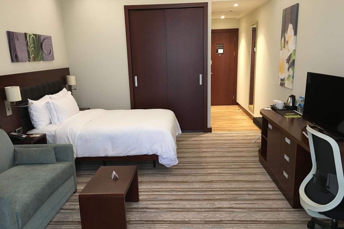 A hotel room with a bed, a desk, a chair, a TV, and artwork on the walls.