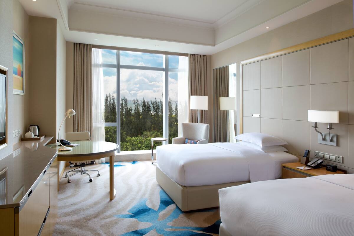A hotel room with a large bed, a desk, a chair, and a view of the outdoors.
