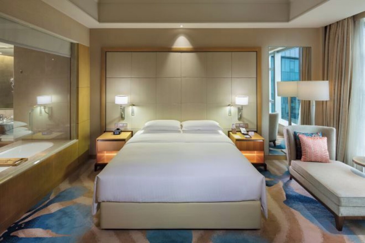 Una habitación de hotel con una cama grande, dos mesitas de noche con lámparas, un sofá, una silla y un espejo amplio.