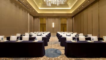 Un salón de conferencias con filas de mesas, sillas y botellas de agua, con una alfombra estampada y un diseño de techo moderno.