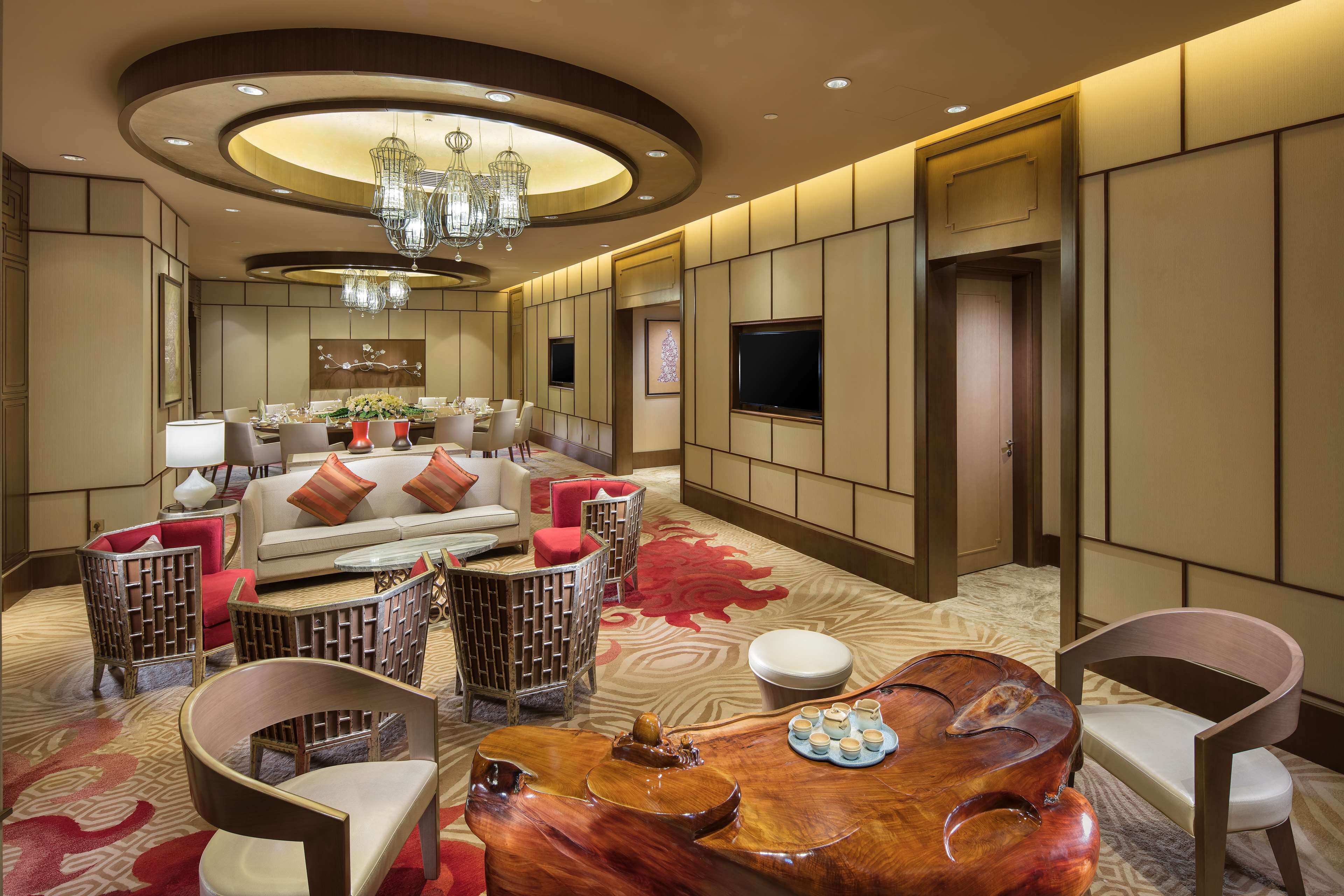 A modern hotel lobby with a round seating area, a wooden coffee table, and a chandelier.