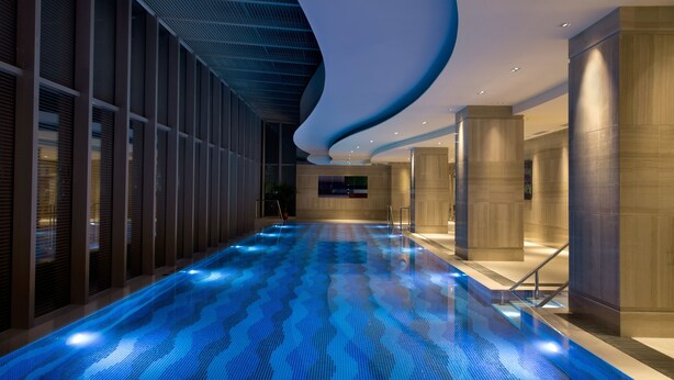 Una piscina interior moderna con un diseño de techo ondulado y suelo iluminado en azul.