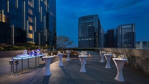 Terraza en la azotea con mesas dispuestas para un evento formal, con vistas a un paisaje urbano al atardecer.