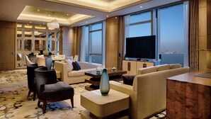 Habitación de hotel moderna con televisor grande, asientos cómodos, un jarrón decorativo y vistas a la ciudad.