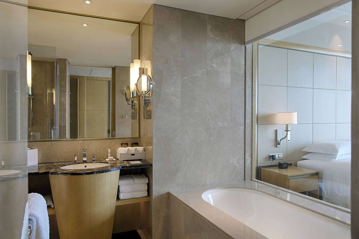A modern bathroom with a large mirror, two sinks, a bathtub, and a vanity with a towel rack.