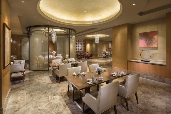 A spacious dining area with a large round table, multiple chairs, and a modern chandelier.