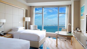 Habitación de hotel con dos camas, un escritorio y vista al océano.