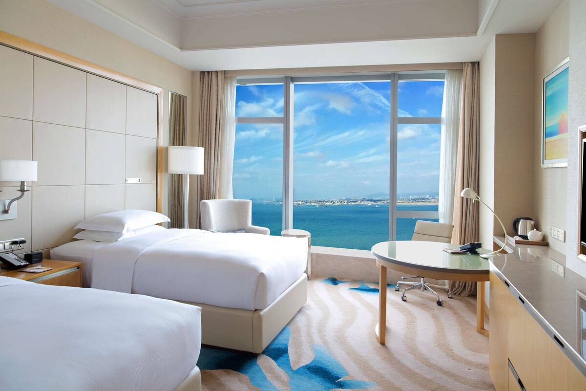 A hotel room with two beds, a desk, and a view of the ocean.