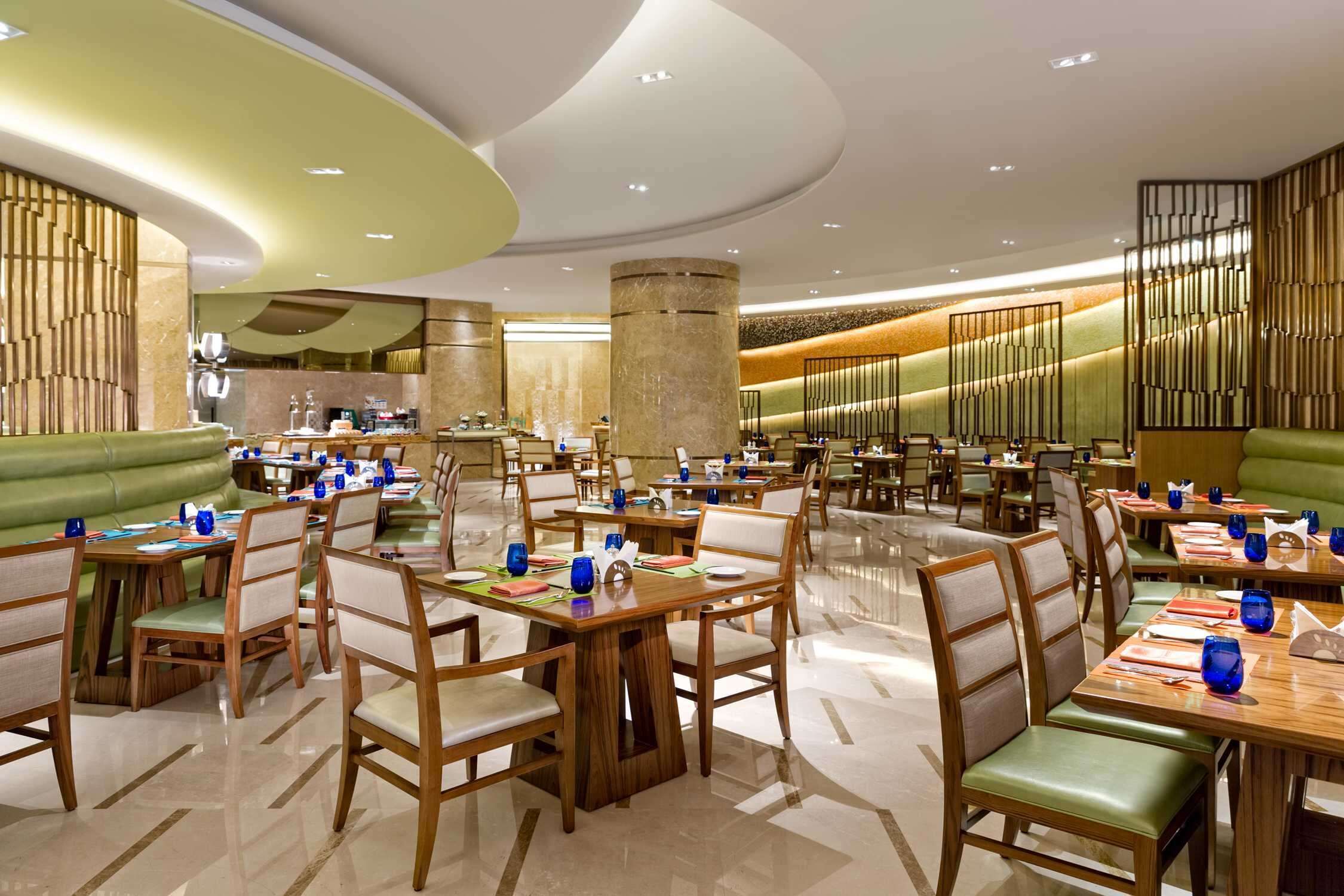 Een ruime restaurantruimte met meerdere eettafels en zitjes, uitgevoerd in een modern design met een gebogen plafond en een centrale pilaar.