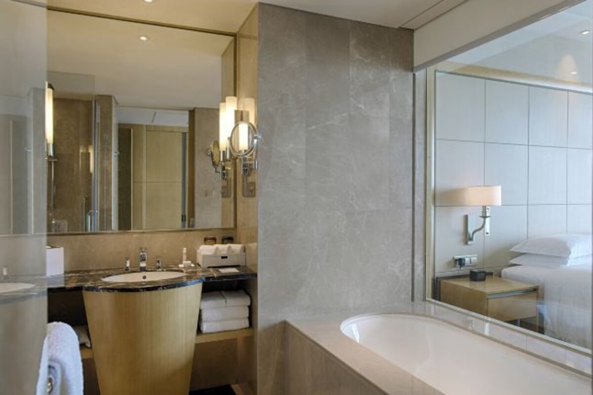 Un baño moderno con un espejo grande, dos lavamanos, una bañera y un mueble de tocador con toallas.