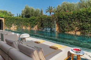 A poolside area with lounge chairs, a small table, and a bowl of fruit. - Mandarin Oriental, Marrakech (Marrakech)