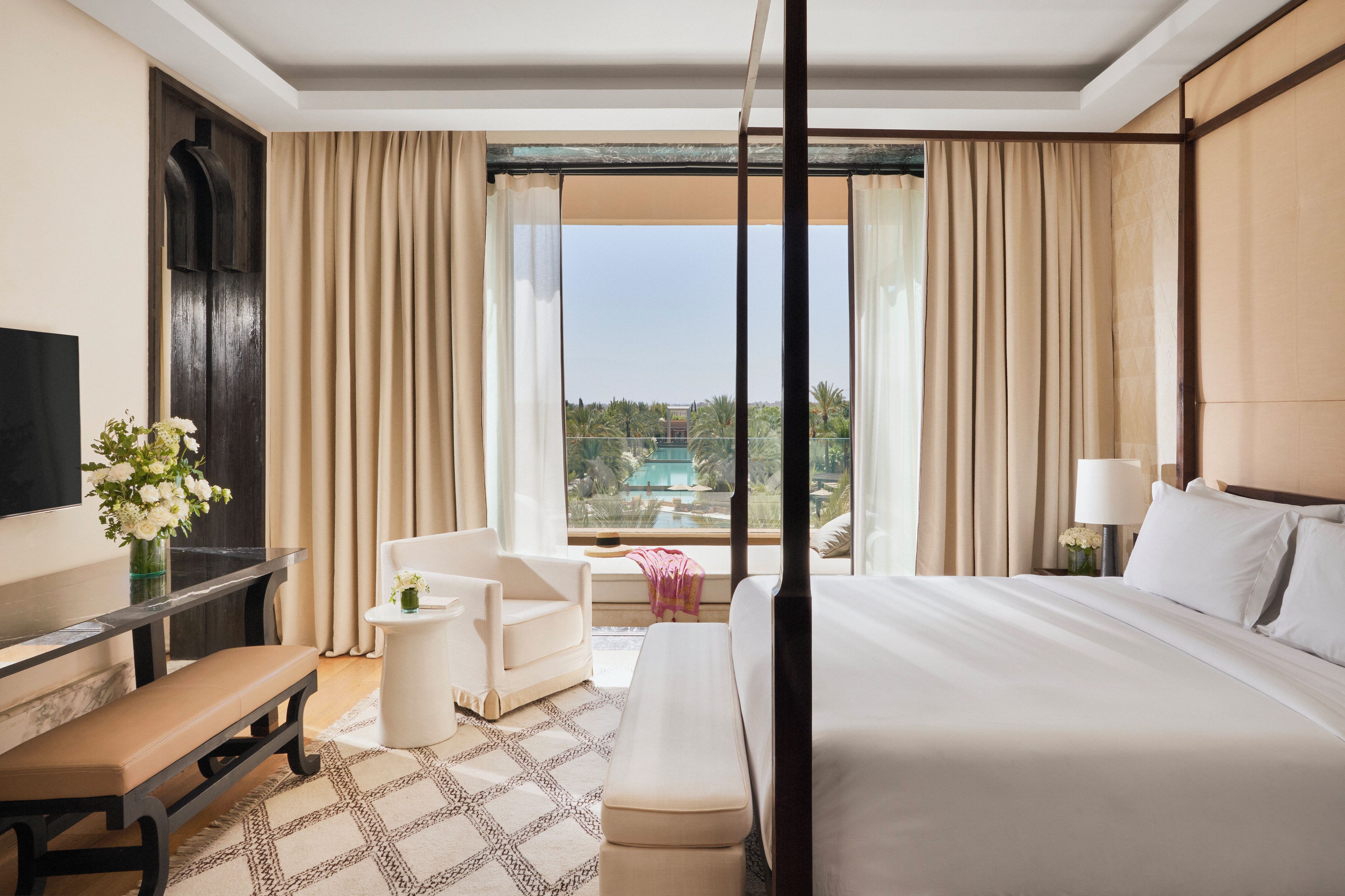 Habitación de hotel con cama, televisión, escritorio, silla, una mesita y vistas a una piscina y jardines.