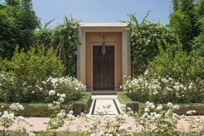 Un bâtiment doté d’une porte en bois sombre, entouré d’une végétation luxuriante et de fleurs blanches.