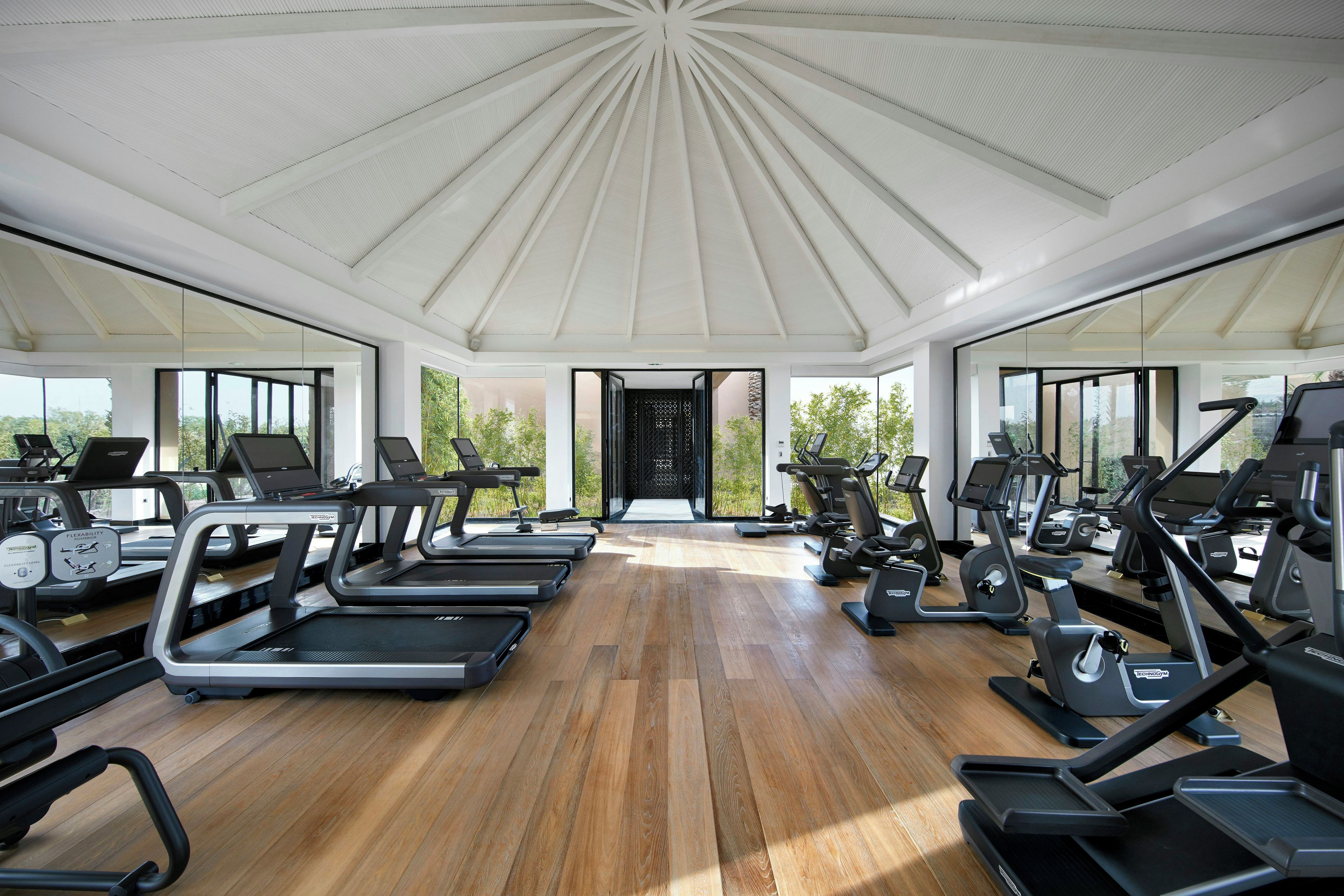 A gym with treadmills, stationary bikes, and elliptical machines arranged in rows.